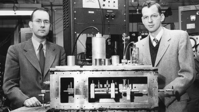 Researchers standing beside an early computing apparatus